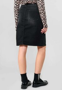 Zwarte denim rok met een getailleerd ontwerp, halverwege het bovenbeen, twee achterzakken en een lichte slijtage aan de onderrand. Gepaard met zwarte schoenen en gestructureerde sokken.