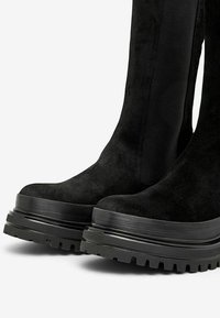 Černé semišové vysoké boty po kolena s tlustou černou platformou, mají hladký povrch a postranní elastické panely pro snadné obouvání.