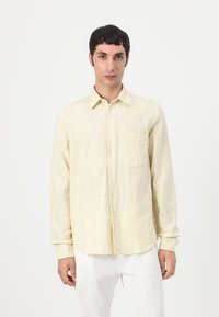 Cămașă butonată de un galben deschis, cu un model texturat în dungi, mâneci lungi, un buzunar pe piept și material moale, asociată cu pantaloni albi.