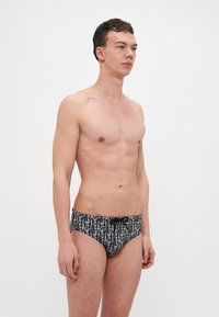 Trunchi de baie negri, cu un model repetitiv de text alb, realizat din material elastic. Talie elastică pentru o fixare sigură.