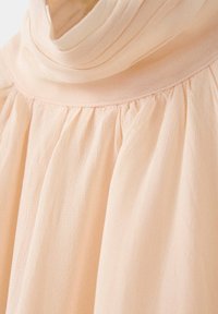 Gros plan sur un tissu beige clair avec des plis froncés sous un col ou un décolleté lisse et plié.