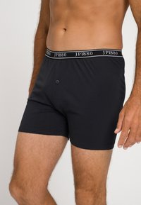 Boxer shorts de algodón negro con cintura elástica, adornados con texto blanco, cierre frontal con botón y un diseño ajustado.