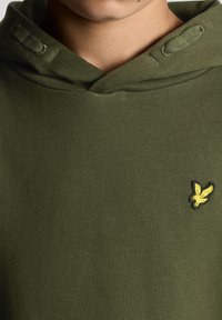 Felpa verde oliva realizzata in tessuto morbido, con un fit rilassato, cappuccio con cordoncino e un logo giallo ricamato sul petto.