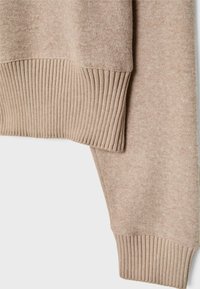 Beżowa dzianina z bliska, ukazująca prążkowany dół i mankiet rękawa, o drobnej fakturze i miękkim materiale.