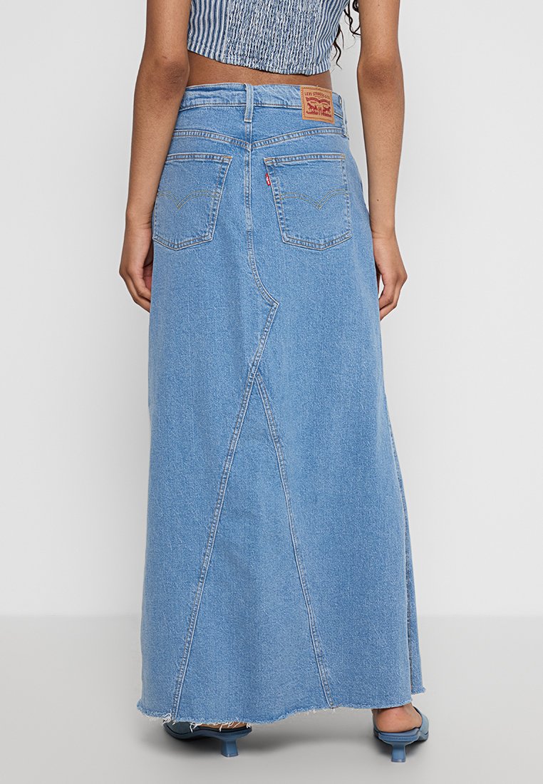 Falda maxi de mezclilla azul clara con cintura alta, bolsillos traseros y dobladillo ranurado y en ángulo. Presenta borde deshilachado y sutiles detalles de costura.
