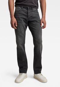 Vaqueros de mezclilla gris oscuro con un corte recto, cinco bolsillos y una sutil textura desgastada. Combinados con zapatillas de color claro.