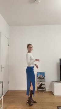 Hosszú ujjú fehér blúz kék, testhez simuló szoknyával, oldalrészes kivágással, kiegészítve fényes fekete térdig érő csizmával.
