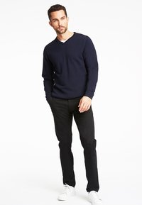 Maglione blu navy a maglia con scollo a V, maniche lunghe, abbinato a pantaloni neri e sneakers bianche, che mette in mostra un design casual e aderente.