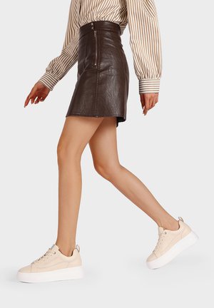Mini gonna di pelle marrone scuro abbinata a scarpe da ginnastica beige con suole spesse e testurizzate e punta arrotondata, che mettono in mostra un design elegante.