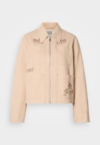 Ανοιχτό καφετί κοντό μπουφάν φτιαγμένο από βαμβάκι με δύο μπροστινές τσέπες. Διαθέτει κεντημένα σχέδια ενός μονόκερου και λουλούδια. Ασημένιο φερμουάρ.