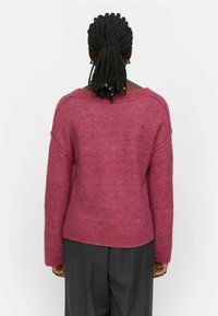 Magenta sviiter pehmes, tekstureeritud kudumisest, laia dekoltee, langenud õlgade ja sooniku äärega. Koos hallide pükstega.