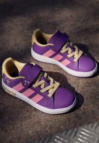 Fioletowe trampki z różowymi paskami, żółtymi akcentami, teksturowaną syntetyczną cholewką, paskiem na rzep i wzorami serc. Biała gumowa podeszwa.