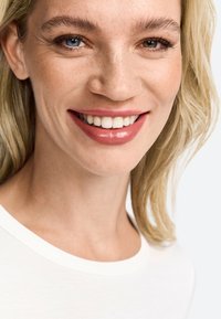 Lähedusvõte inimesest, kellel on heledat nahka ja blondid juuksed, kandes valget särk. Neil on lai naeratus ja looduslik meik, mis rõhutab nende näojooni.