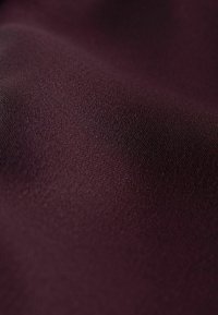 Primo piano di un tessuto viola scuro, liscio, con una trama fine e una leggera riflessione della luce sulla superficie dolcemente curvata.