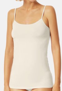 White tank top with thin adjustable straps, seamless design, soft cotton material, and a slightly fitted shape, suitable for layering.