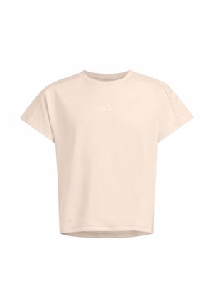 Mujer joven de pie con las manos en los bolsillos, vistiendo una chaqueta negra, camiseta beige, pantalones cortos negros hasta la rodilla, calcetines blancos y zapatillas negras.