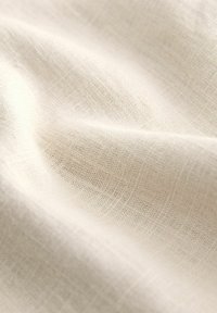 Tela beige claro con una superficie suave y texturizada y un sutil patrón de tejido, mostrando pliegues suaves y un drapeado liso.