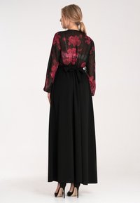 Maxi sukienka z przezroczystą czarną koronką z czerwonymi różami, długimi rękawami i czarną marszczoną spódnicą, zdobiona wiązaniem w talii.