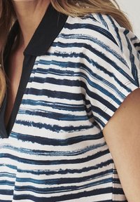 Chemise à manches courtes avec col, présentant des rayures horizontales bleues et blanches, une texture lisse et un accent de col foncé.