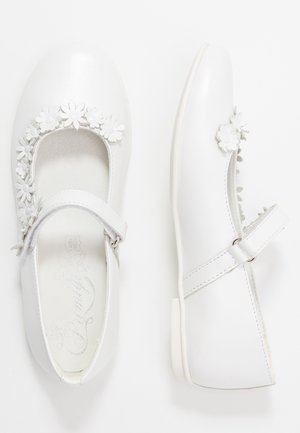 Białe skórzane buty typu Mary Jane z aplikacją w kształcie kwiatu wokół wycięcia oraz regulowanym paskiem z srebrną klamrą. Płaska podeszwa.