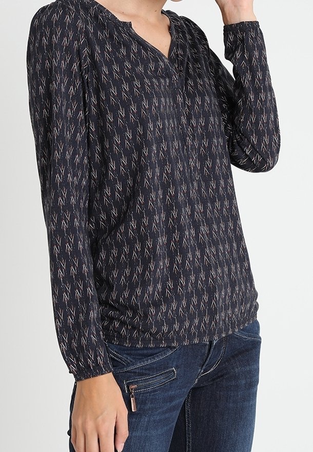Marinblå blus med lång ärm och subtilt zigzag-mönster i ljusa färger. Har delad urringning och draperade manschetter. Mjukt, lätt tyg.