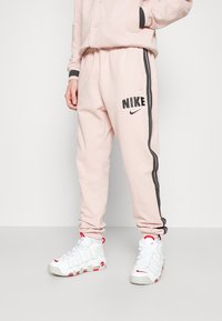 Ljusrosa Nike sweatpants med grå sidostripes och logga, med elastisk midja och ärmslut. Matchas med vita sneakers med röda accenter.