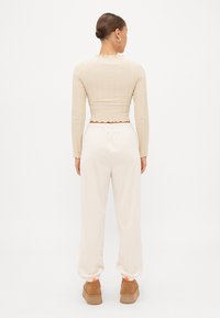 Top cropped de manga longa bege com bainha ondulada, combinado com calças jogger de cintura elástica em creme. Sapatos de plataforma castanhos com pormenores laranja completam o visual.