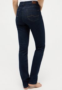 Mørkeblå denimjeans med rett bein, med et lærmerke på midjebåndet og to baklommer med diskret søm.