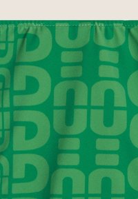 Vihreä kangas, jossa on suuri, toistuva vaaleanvihreä abstrakti kuvio, joka sisältää kaarevia ja suorakulmioita muotoja, sileä pinta ja joustava vyötärö.