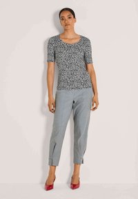 Schwarzes und weißes Leopardenmuster angepasstes Oberteil mit kurzen Ärmeln, kombiniert mit grauen, taillierten Hosen mit Umschlägen und roten spitzen Absatzschuhen.