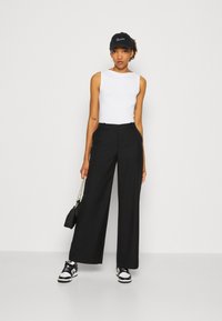 Sorte brede bukser parret med en hvid ærmeløs top. Outfit'et inkluderer en sort kasket og sorte og hvide sneakers, samt en lille håndtaske.