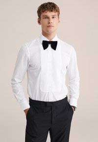 Balta smokings krekls ar pleķētu priekšpusi, melnu tauriņu un garām piedurknēm ar pogām. Valkāts ar melnām biksēm.