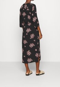 Mustakukkaista mekkoa, jossa on kolmanneksen hihat, pinkki-valkoisella kukkakuviolla ja sivureiällä. Yhdistetty vaaleanbeigeihin liukuvasti istuviin sandaaleihin.