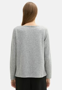 Grijze lange mouwen trui met een geribbelde textuur. De achterkant heeft een ronde halslijn en een ontspannen pasvorm, gecombineerd met zwarte broek.