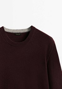 Burgundinpunainen neulepusero, jossa on klassinen pyöreä pääntie, kontrastivärinen harmaa ribbineuloskaulus ja pehmeä, teksturoitu kangas.