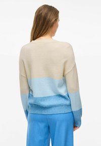 Lekki, wielokolorowy sweter w odcieniach beżu i niebieskiego, charakteryzujący się luźnym krojem oraz prążkowanym dekoltem, z bocznymi rozcięciami u dołu.