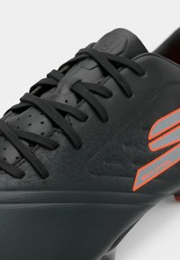 Black soccer cleat with textured surface, black laces, and an orange accent. Features a streamlined design and a smooth finish.