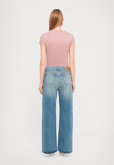Light pink short-sleeve top paired with wide-leg blue jeans. The jeans have a gradual fade and a tan leather patch at the back.