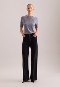 Grauer Kurzarmpullover kombiniert mit hoch taillierten, schwarzen, weit geschnittenen Jeans mit Knopfverschluss und eleganten schwarzen spitzen Absatzschuhen.