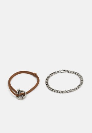 Brunt læderarmbånd med en sølvspænde og cirkulær løkke, ved siden af et sølv kædearmbånd med en hummerlås og sammenkoblede led.