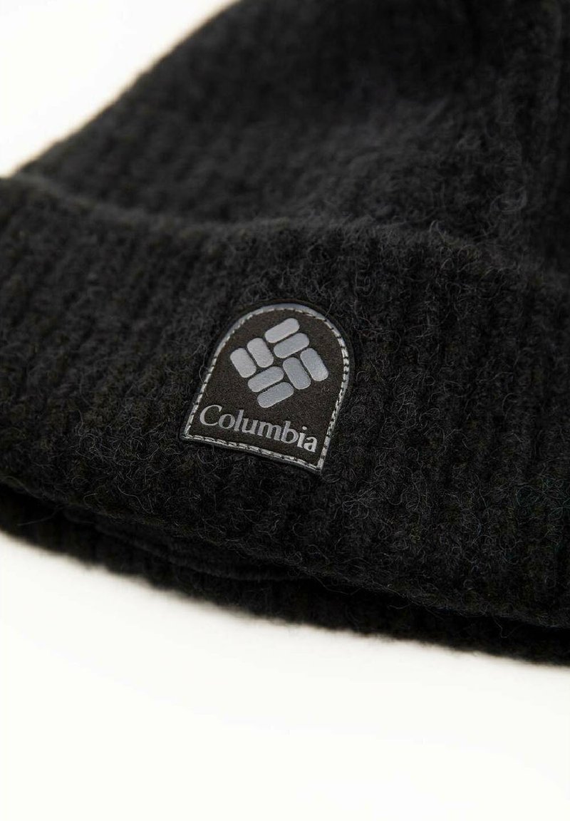 Gorro de punto negro hecho de lana suave, con un logo de Columbia en un parche redondeado. La textura es acanalada con un puño doblado.