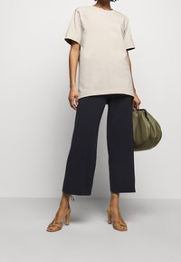T-shirt beige a maniche corte, vestibilità rilassata; pantaloni a gamba larga blu navy; tacchi a strappo marrone chiaro; borsa verde texture; design minimalista nel complesso.