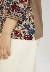 Topp med kort ärm i beige tyg med ett blommönster i röd, blå och vit, kompletterad med en enfärgad brun kant.