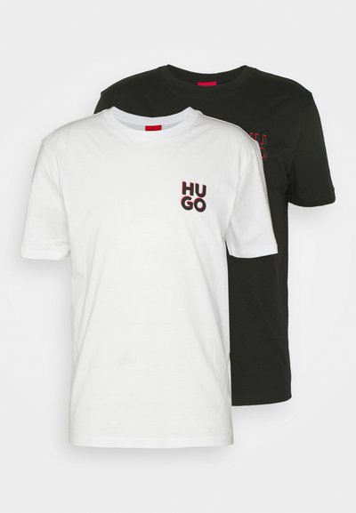 Deux t-shirts à manches courtes, en blanc et en noir. Le t-shirt blanc arbore un logo "HUGO" avec des accents rouges sur la poitrine gauche. Fabriqué en coton.