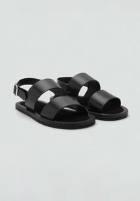 Sandalias negras con dos correas anchas y una correa trasera, hechas de material suave. Suela de goma plana, diseño minimalista y hebilla ajustable.