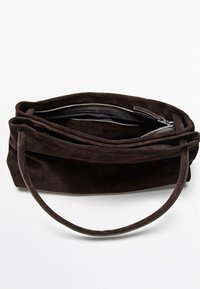 Sac à main en daim marron foncé avec une texture douce, fermeture éclair et une fine sangle. L'intérieur présente une poche et un compartiment spacieux.