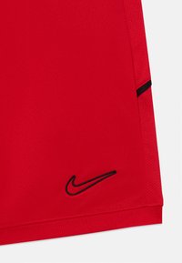 Șorturi atletice roșii, confecționate dintr-un material neted, având un logo Nike negru la tiv și o dantură neagră contrastantă pe margine.