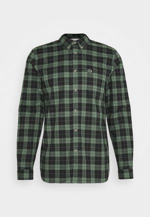 Chemise à manches longues à carreaux verts et noirs, à boutons, avec un col boutonné et un petit logo brodé sur la poitrine.