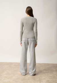 Hellgrauer, gerippter Strickpullover mit langen Ärmeln, kombiniert mit weit geschnittenen, hellgrauen Denim-Jeans. Der Pullover hat einen runden Halsausschnitt und eine taillierte Silhouette.