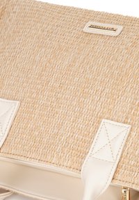 Geweven stro handtas met een beige exterior, witte leren accenten en een gouden logo-label. Voorzien van platte handvatten en een gestructureerd oppervlak.